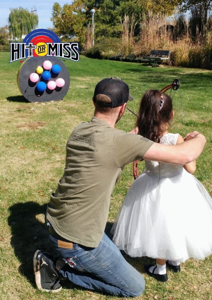 Young girl in a white dress learning to shoot a bow